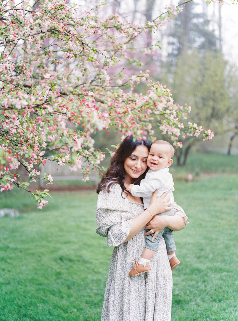 A mother holds her infant son next to a cherry blossom tree at Brookside Gardens in Maryland