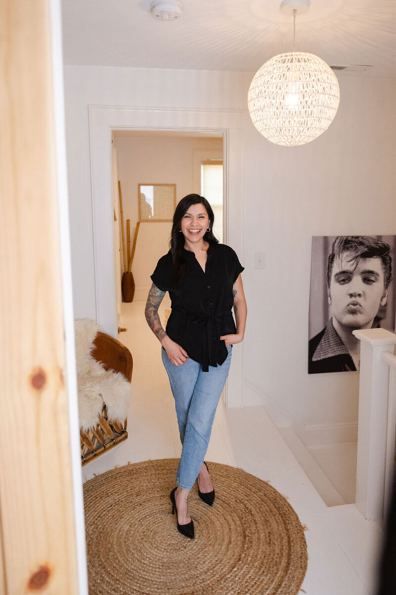 Karen stands at the top of the steps on a jute rug smiling with a portrait of Elvis Presley on the wall
