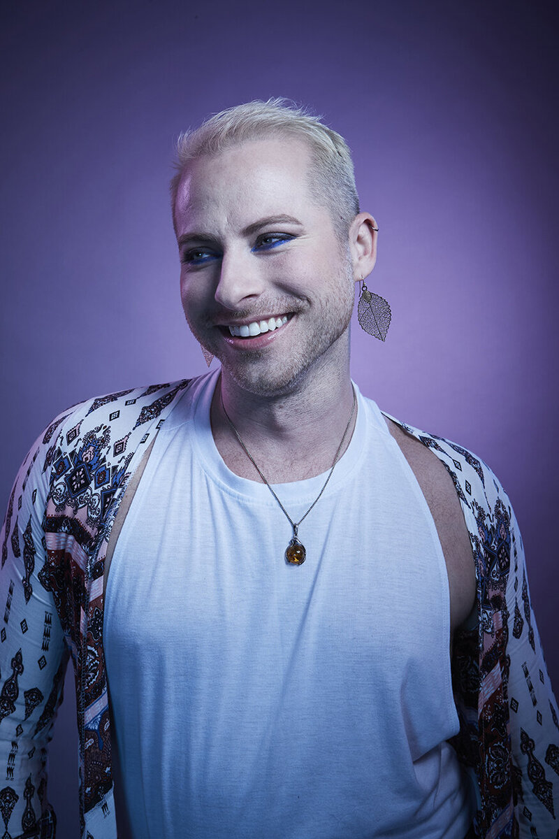 Candid studio portrait of Dain August smiling subtly in a patterned outfit, set against a vibrant backdrop, captured by Ylva Erevall.