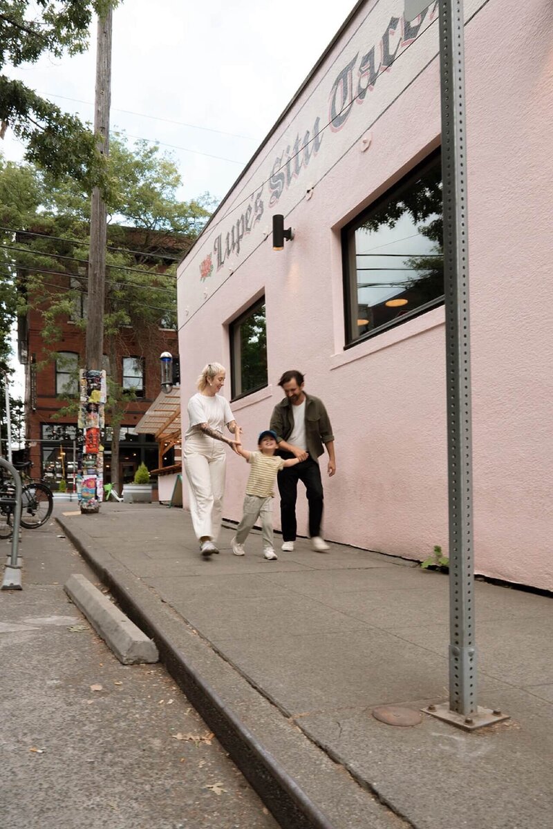 a male and a female running with their little boy with pink taco restaurant backdrop