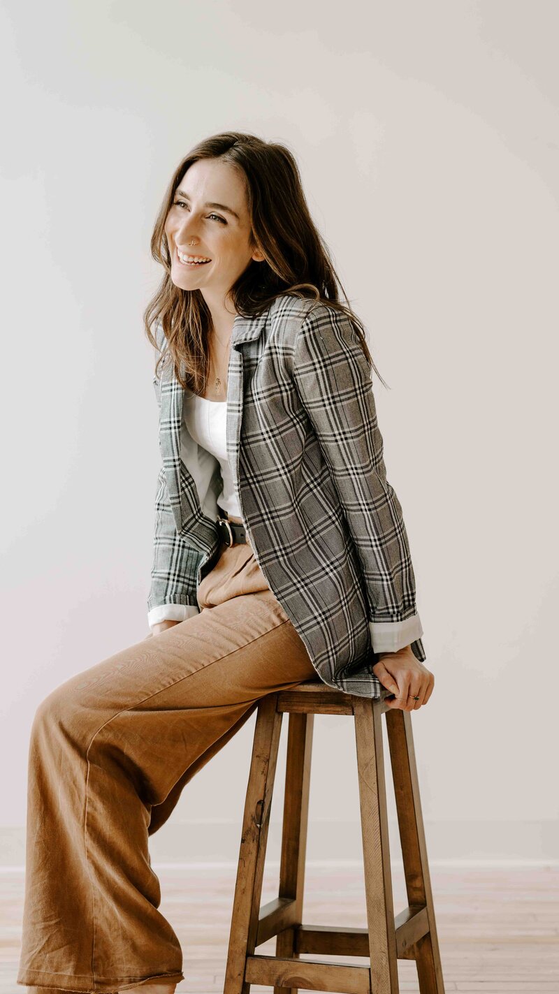 Brand Photographer Lindsay on a stool looking off camera and smiling