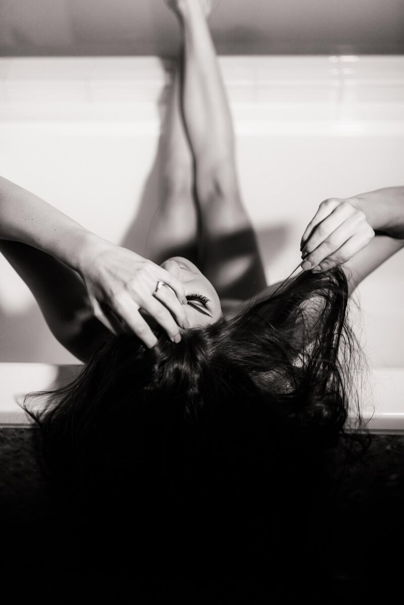 Boudoir photo looking down onto a woman in a bathtub playing with her hair