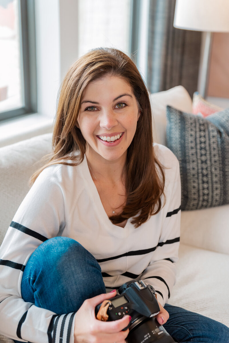 modern headshot of woman holding a camera sitting on a white sofa