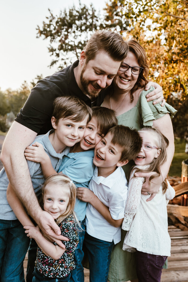Family of 7 squeezing each other tight and laughing together.