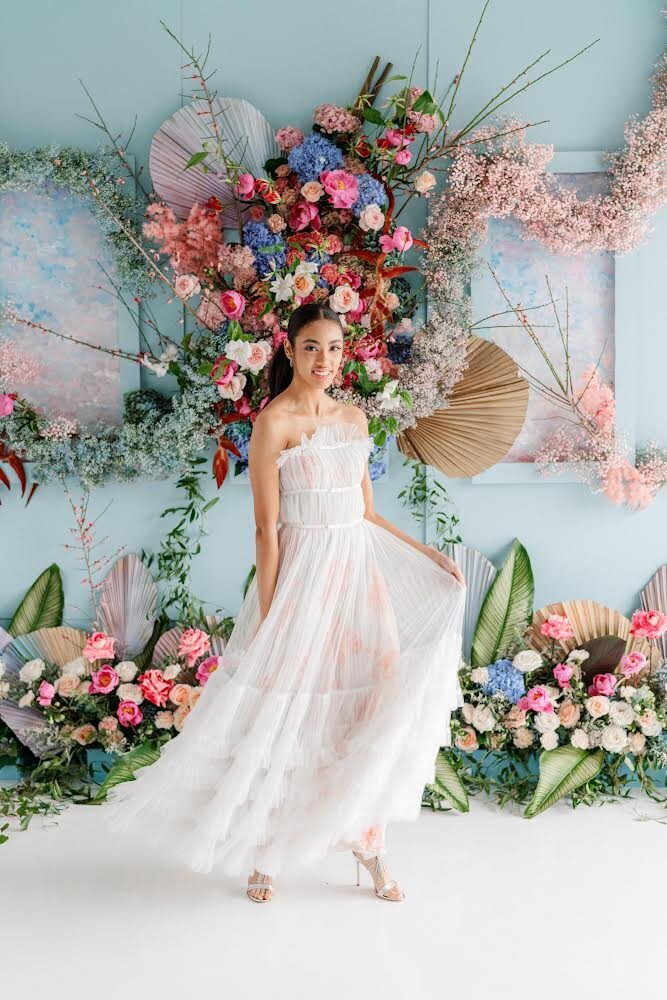 Woman in a white dress standing in front of an elaborate floral backdrop design