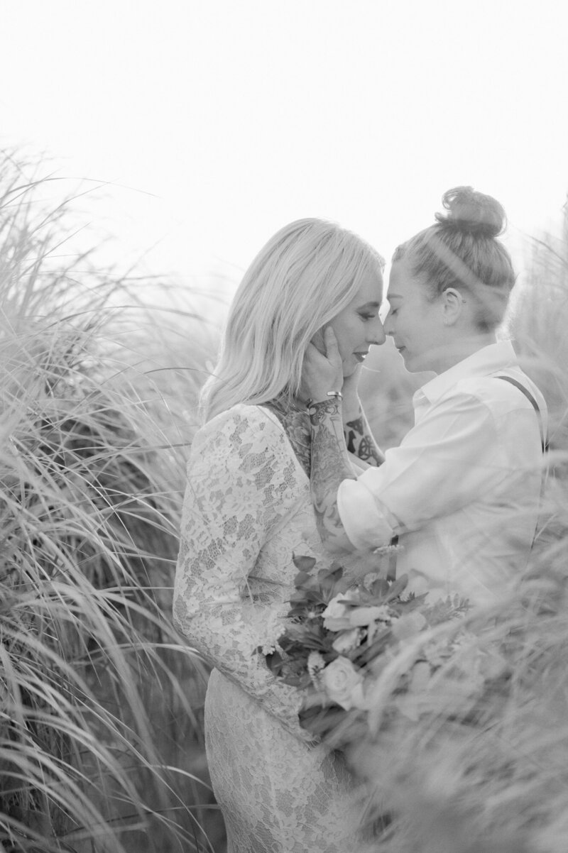 two brides nose to nose in tall beach grass by seattle wedding photographer, lena porter.