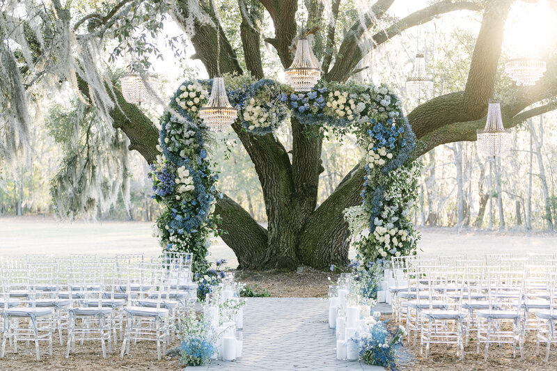 blue floral arch with spanish moss and chandeliers hanging from the trees at hewitt oaks wedding venue captured by savannah wedding photographer magnolia west photography