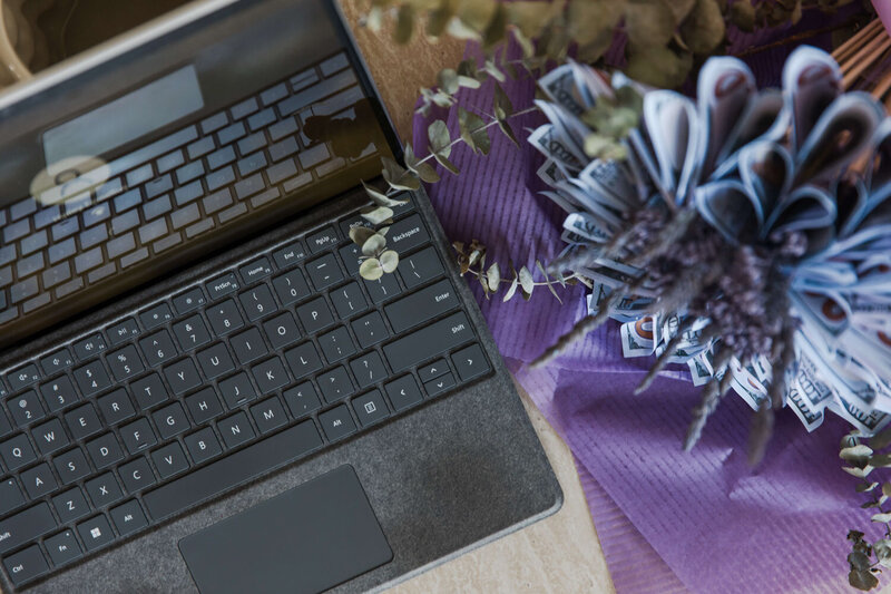 Laptop and bouquet of eucalyptus with money bills. Hailey Ann Co Bookkeeper and somatic money coach for female entrepreneurs.