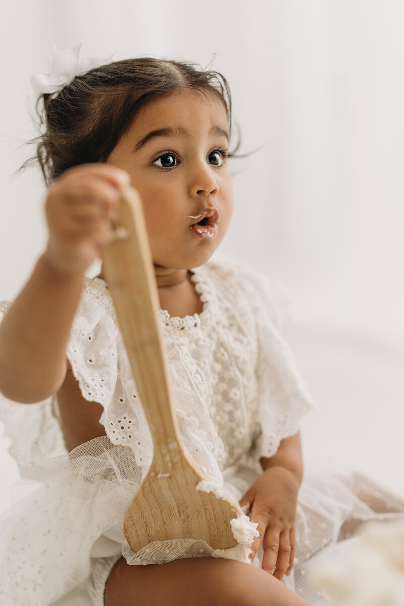 Cake smash with neutral colored outfits and cake falling on floor as baby is eating cake