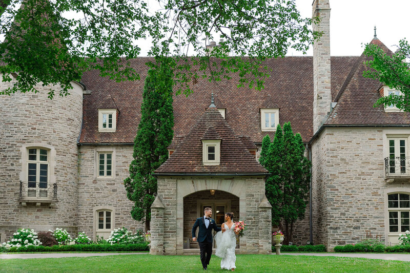 a bride and groom run from the entrance of Eaton Hall in Toronto.  Captured by Ottawa wedding photographer JEMMAN Photography