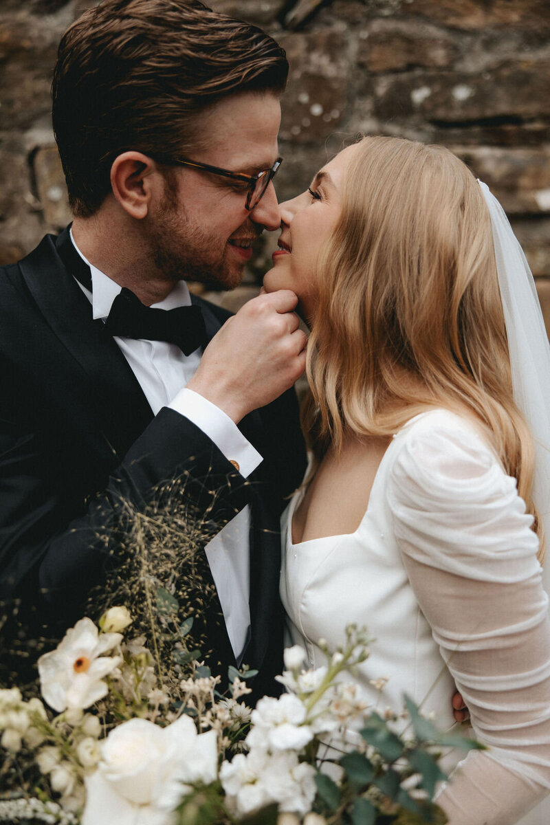 A bride and groom holding each other close, giggling while they kiss