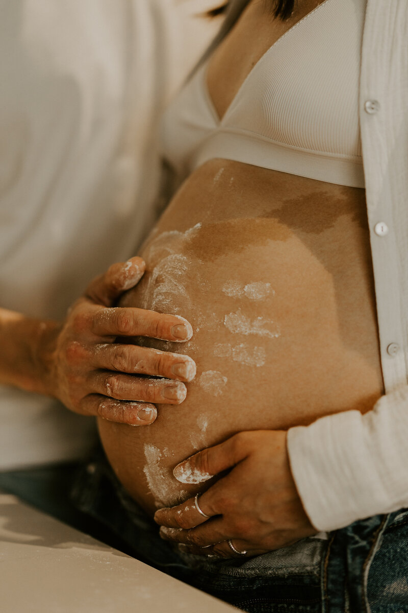 Ventre arrondi d'une femme enceinte de profil, en robe longue blanche, au bord de l'eau, capturée par Laura, photographe grossesse en vendée.