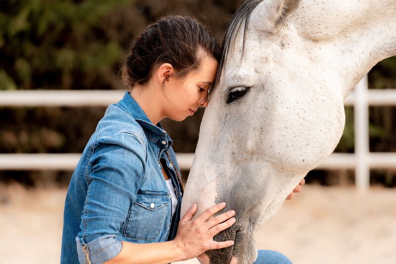 Woman gently touching a white horse’s face during a private equine-assisted learning session