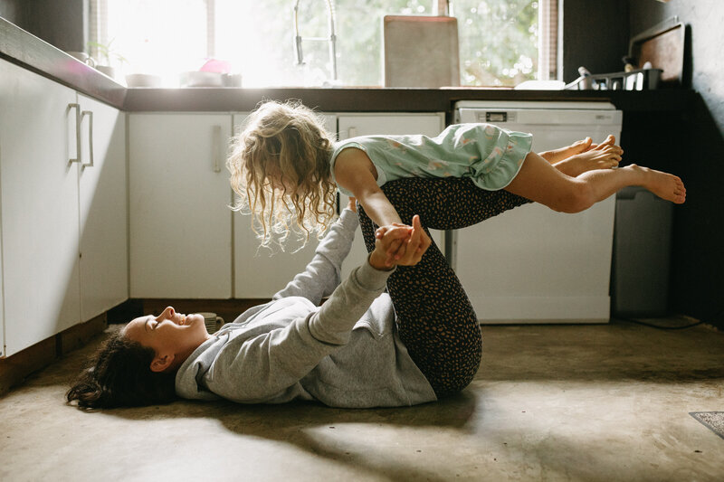A mother and daughter in a kitchen , the light flowing through the windows n a fun candid and joyful moment