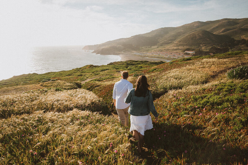 couple holding hands walking on cliffside
