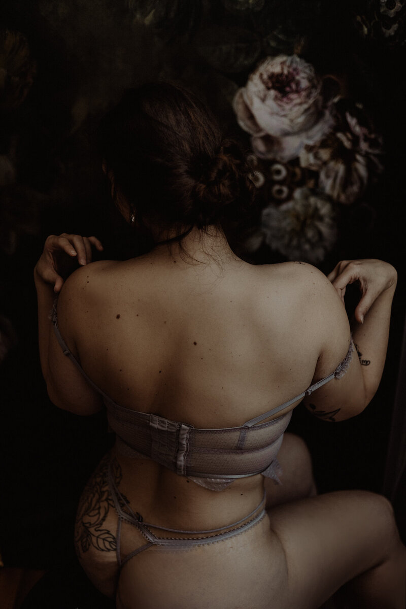 Donna in lingerie di seta chiara, immersa in una luce soffusa e caravaggesca durante un servizio fotografico boudoir di lusso