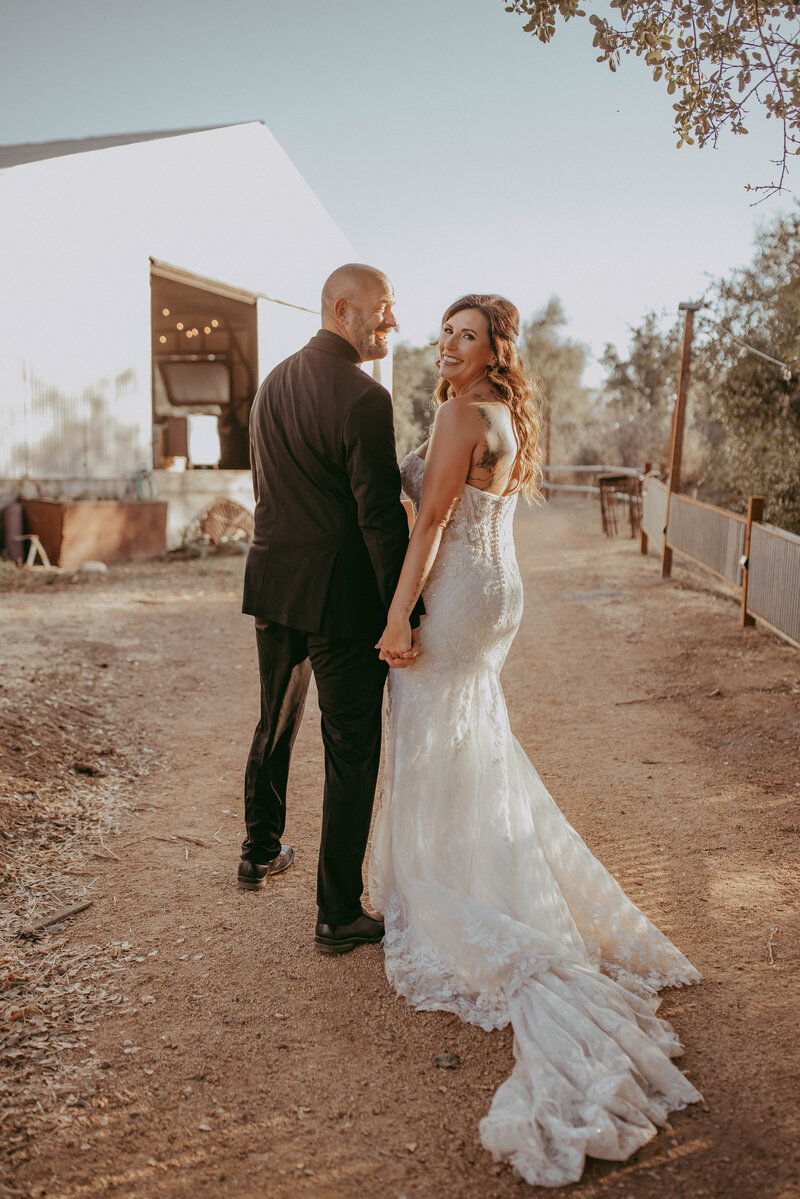 A bride and groom walking towards the [name of venue] venue and looking back other their shoulders after their ceremony. 