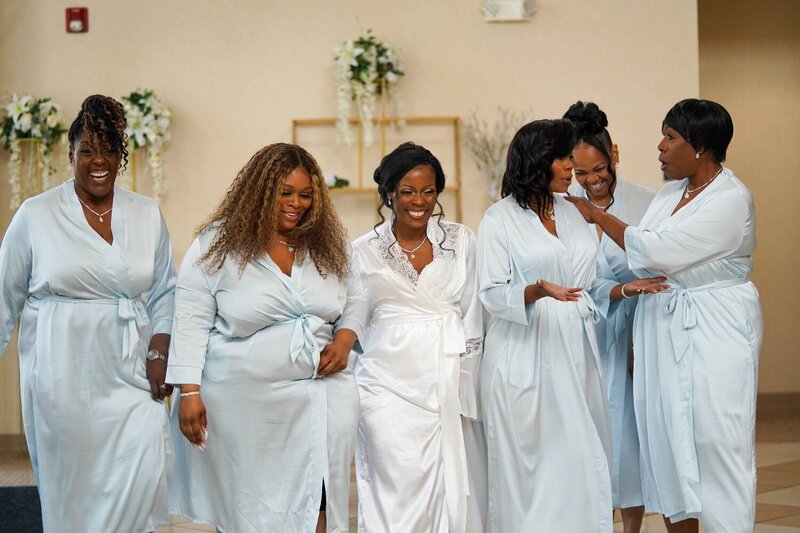Bride laughing with her bridesmaids in matching satin robes during wedding prep at Duneland Falls.