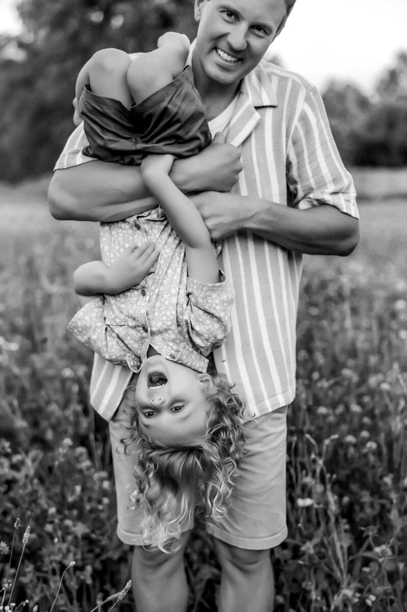 Dad holds his son upside down in flower field while his curly hair hangs in the wind with Kansas City Family Photographer.