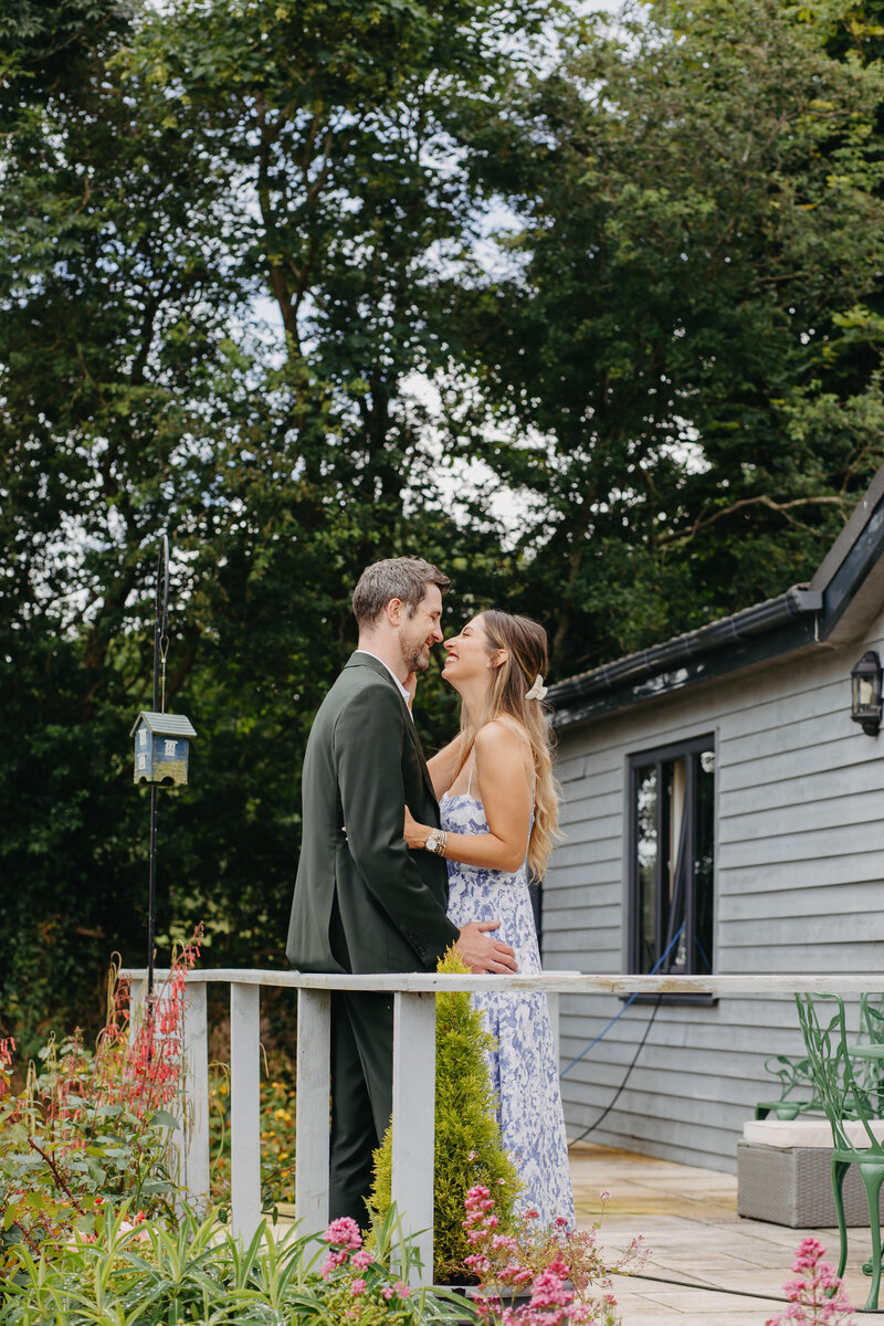 Couple sharing a tender moment on a wooden porch, smiling at each other with love, surrounded by greenery in a peaceful garden setting at College Hill, Ireland 