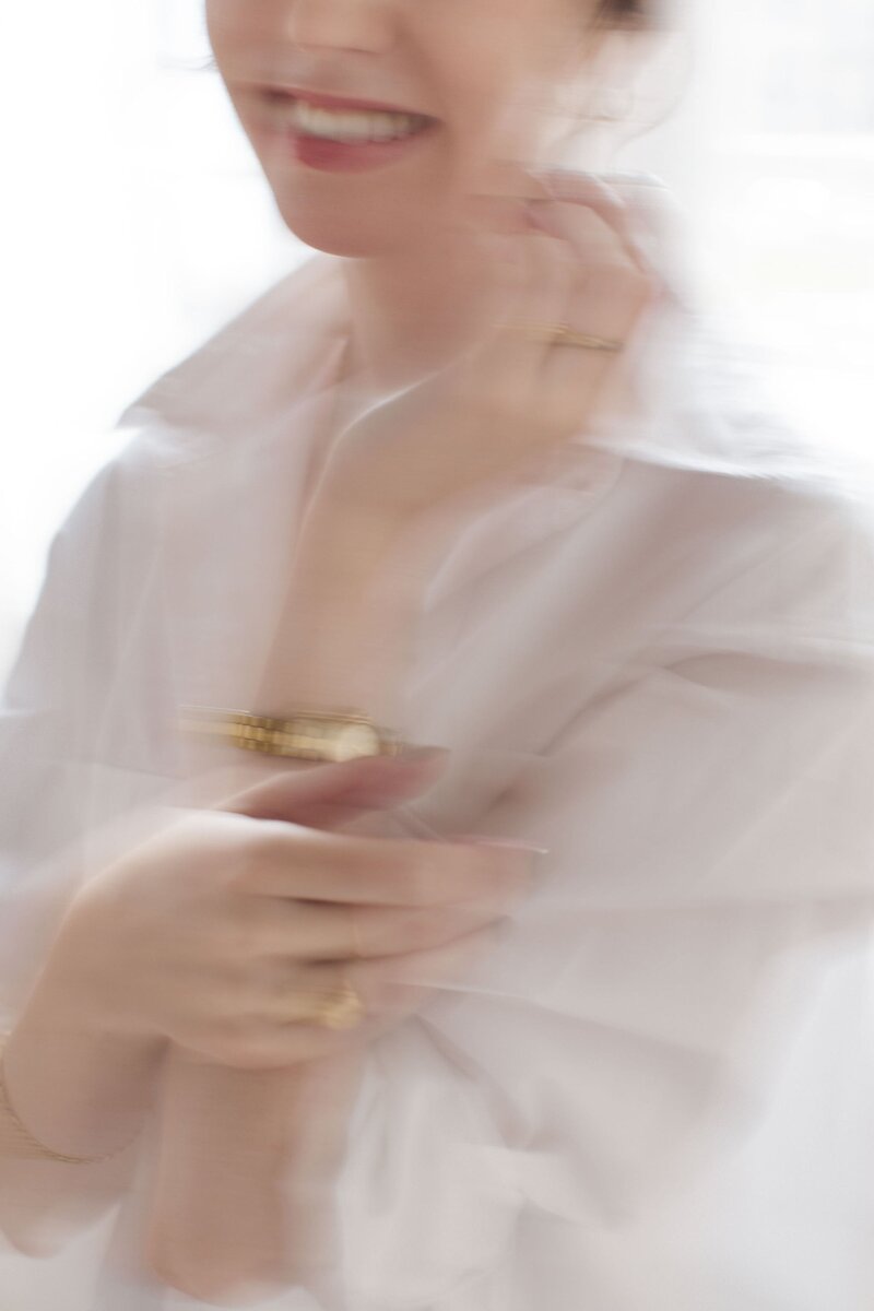 Blurry brand photo of woman wearing gold watch and ring and white blouse