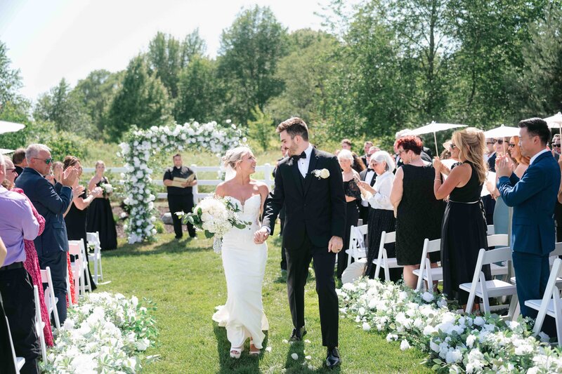 A bride and groom in a black tuxedo come down the aisle after their wedding ceremony.