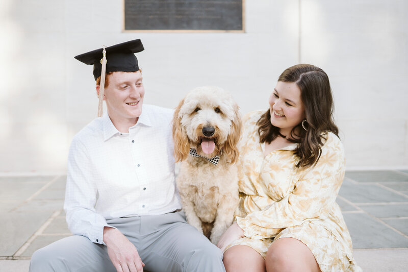 A couple holding their dog with a houndstooth bow at Denny Chimes