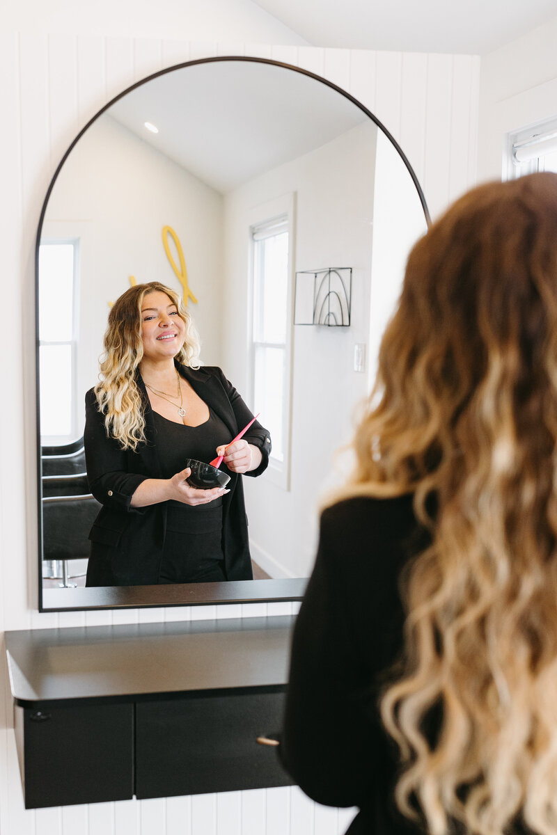 A mirror shot of a professional hair stylist mixing hair dye at Painted Hair Co. Ottawa.