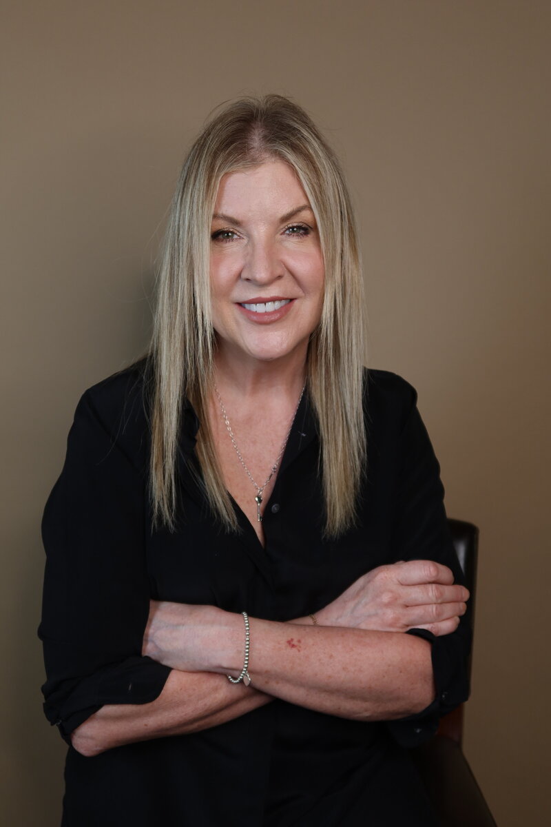Musician Amy Hailstone wearing a black shirt with crossed arms against a beige backdrop.