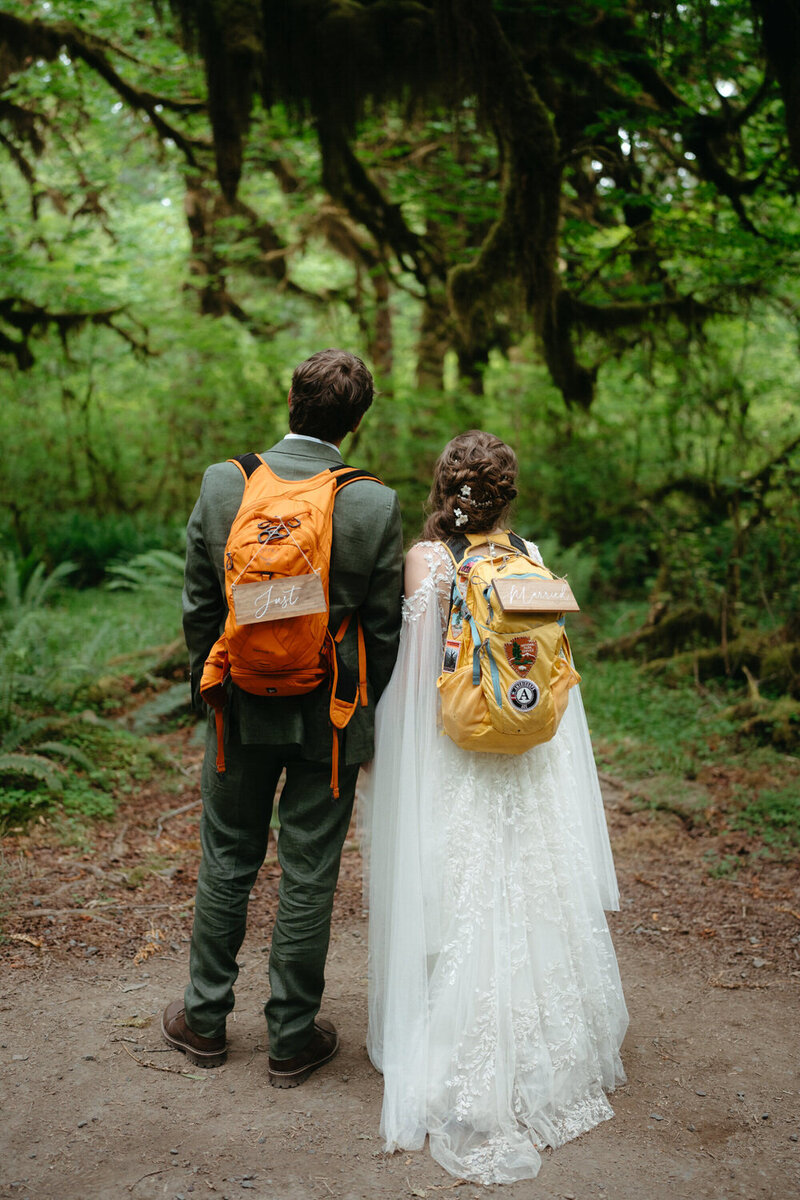 Newly-wed couple stands on the trail during their hiking elopement with backpacks that say "Just Married"