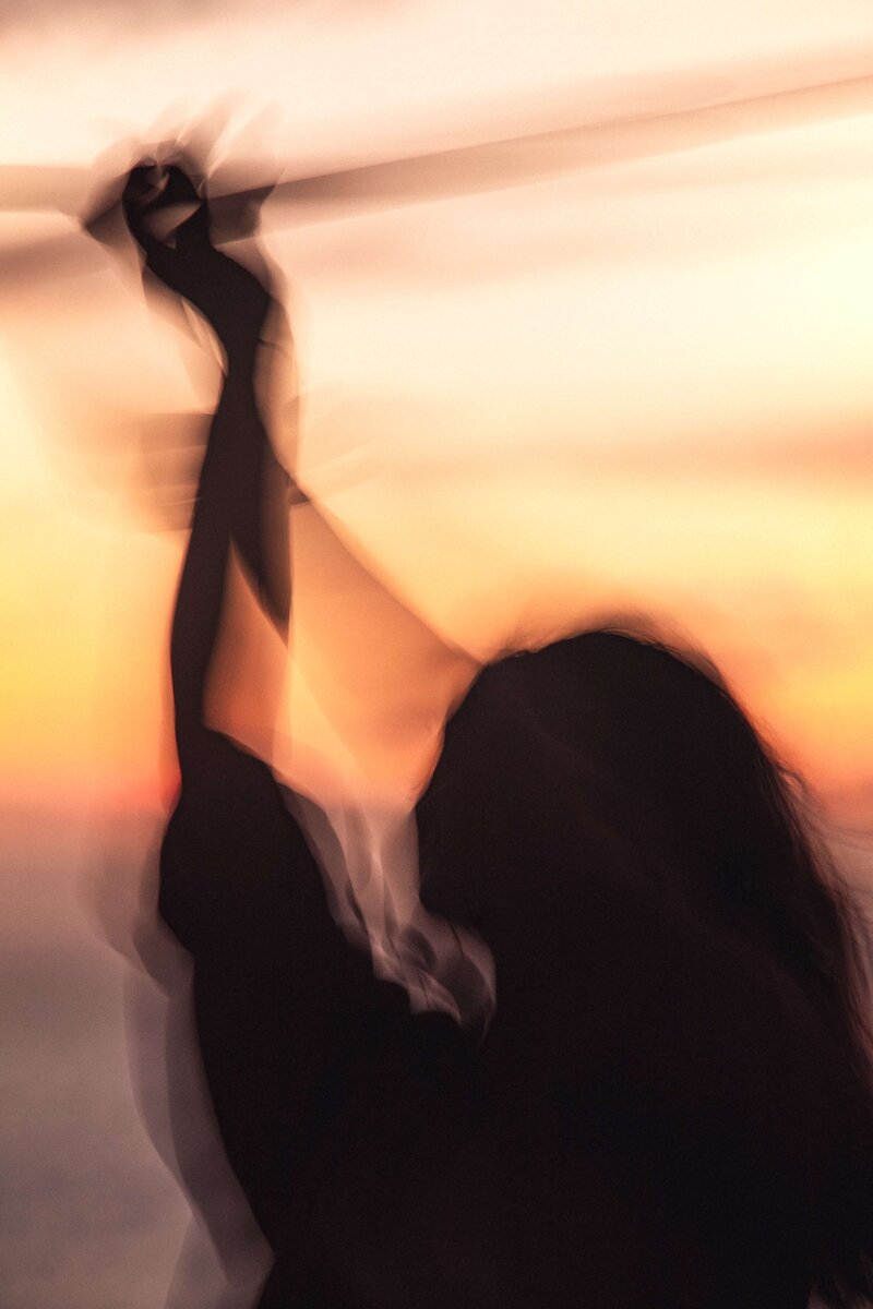 Frau mit nach oben gestreckten Händen bei Sonnenuntergang
