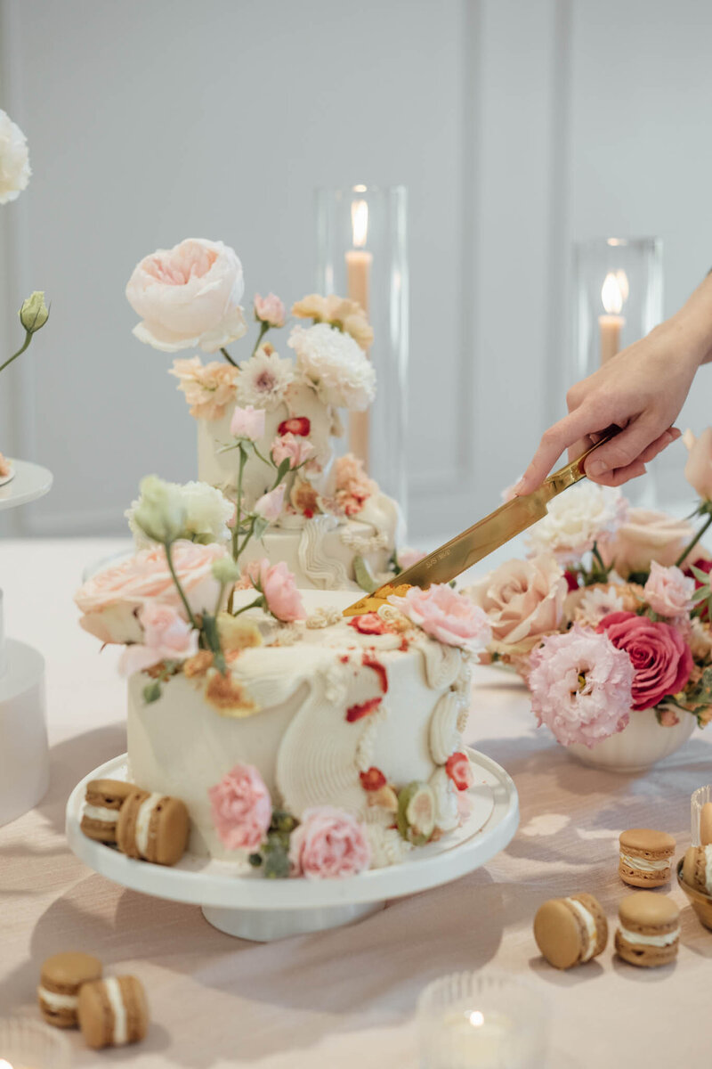 Person's hand cutting a pastel floral cake