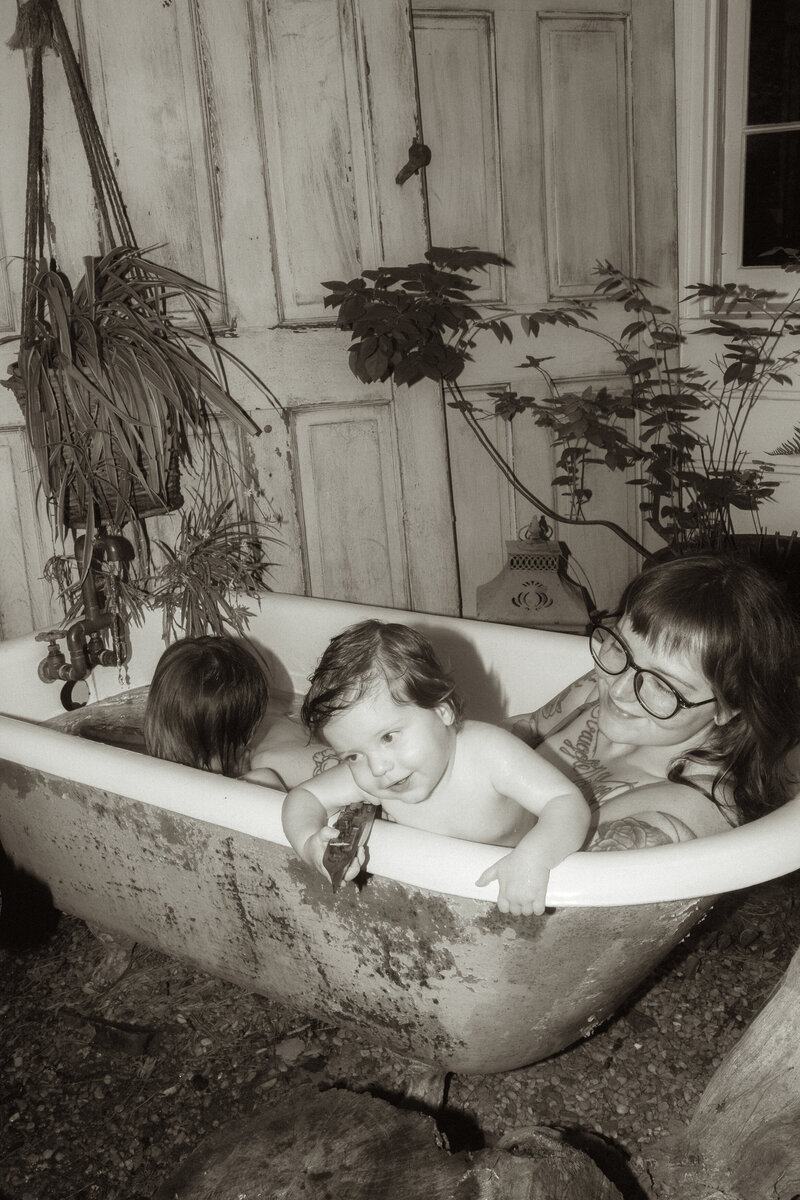 A mom playing in a clawfoot tub with her two young boys. 