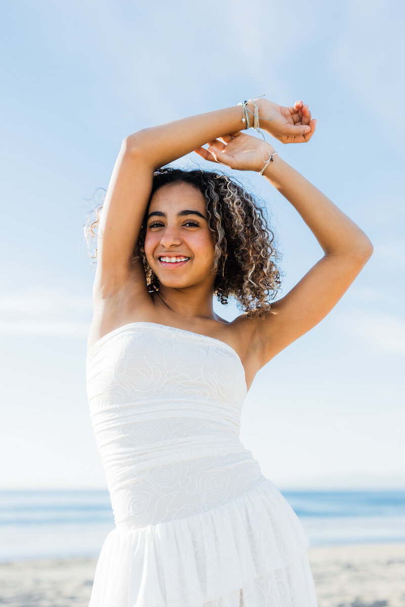 teen-in-cream-dress-holding-her-hands-above-her-head-at-the-beach