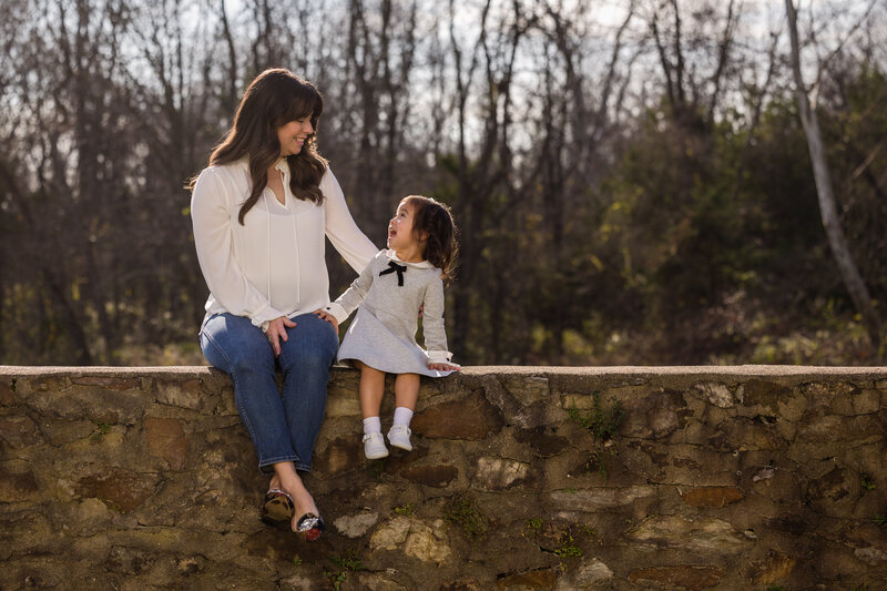 A mom and daughter sharing a heartfelt look while sitting on a stone wall during a family photography mini session in Valley Forge.