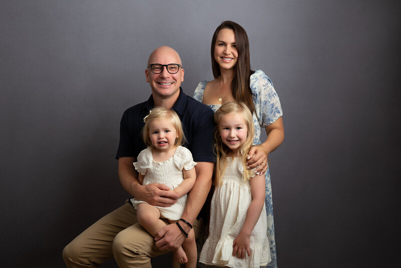 Hampton London studio portrait of a happy family of four with two little  girls on a simple grey background