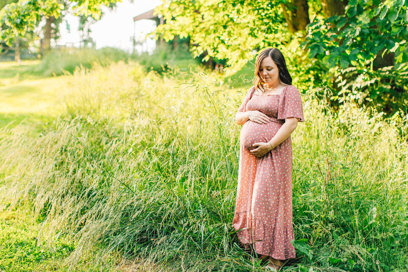 a pregnant woman holding her baby bump in a field
