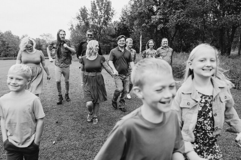 Black and white extended family portrait session of multiple generations looking at each other smiling and running toward the camera. 
