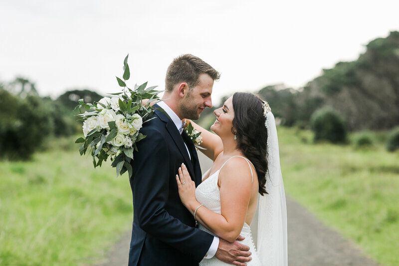 bride and groom snuggling on gravel road at muriwai