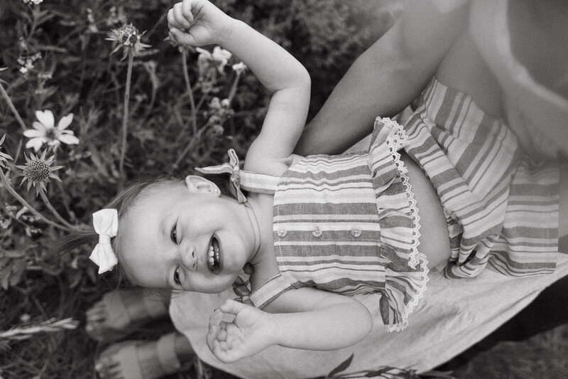 A toddler laughs upside down laying in mom's lap.