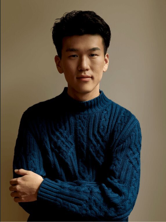 man wearing a blue sweater looking into the camera with a beige wall