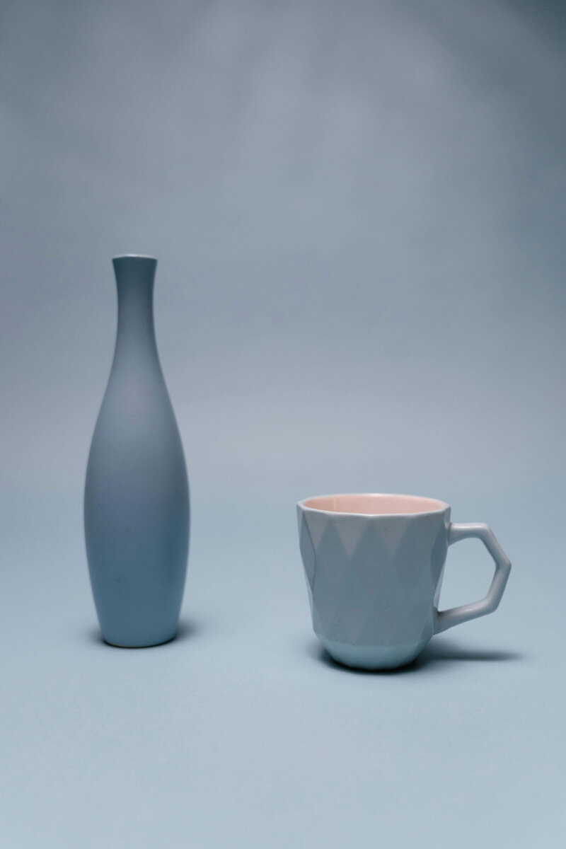 A minimalist composition featuring a sleek blue vase and a matching geometric-patterned teacup with a soft pink interior, set against a pale blue background. This serene and cohesive aesthetic reflects the calm and thoughtful planning often associated with successful vacation fundraising campaigns