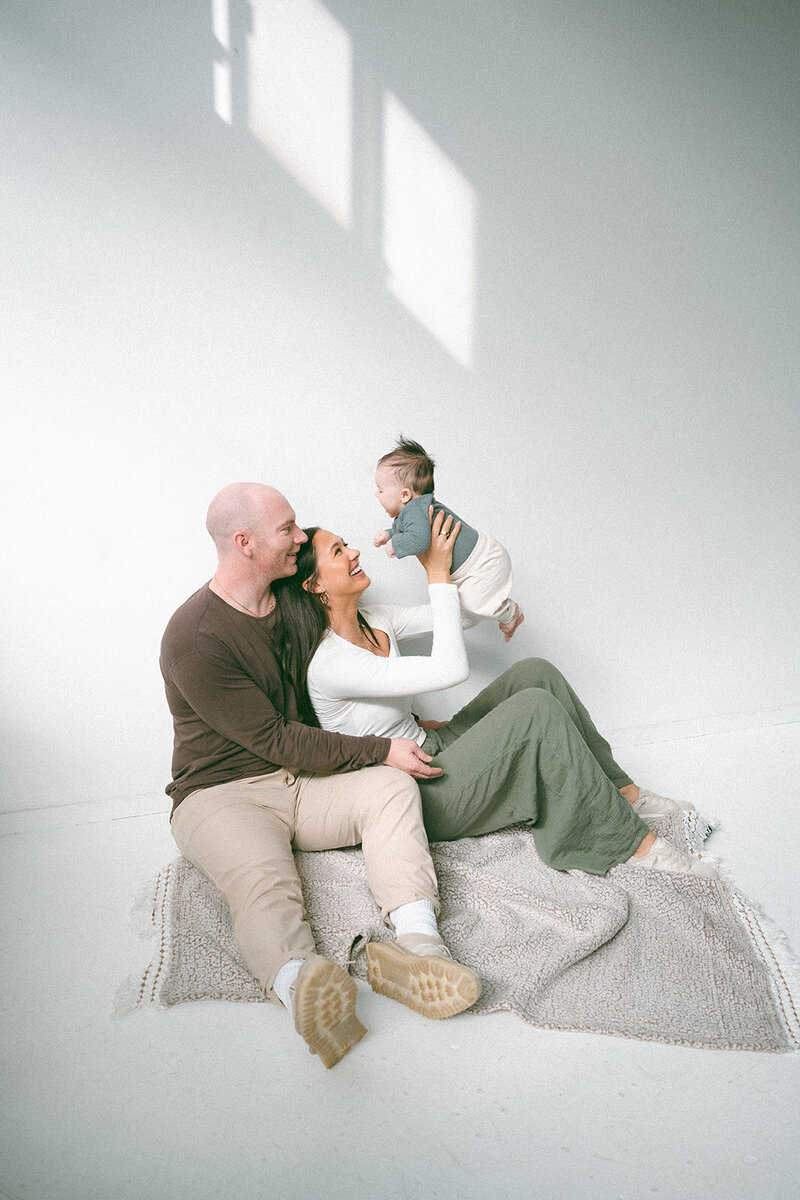 Candid newborn family session in Orange County with parents smiling and lifting baby in natural light.