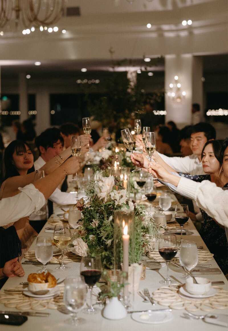 Guests toasting at a floral-decorated banquet table at Hotel del Coronado, designed by Thater Made, a luxury wedding and event producer in San Diego, CA.