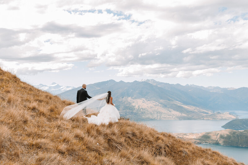 Bride and groom walking into the distance after outdoor wedding at scenic Wanaka mountain venue, with mountains and lakes in the background.