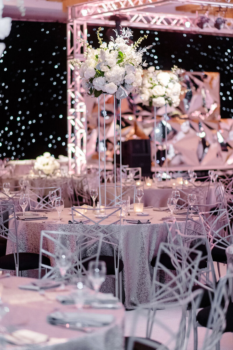 Formal reception setup with silver tables and tall floral centerpieces.