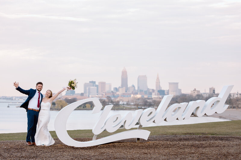 Couple with their arms out posing next to the Cleveland sign