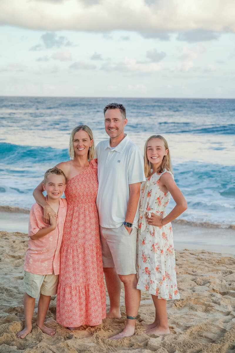 Family smiles on during golden hour light on Shipwreck Beach in Kauai, Hawaii