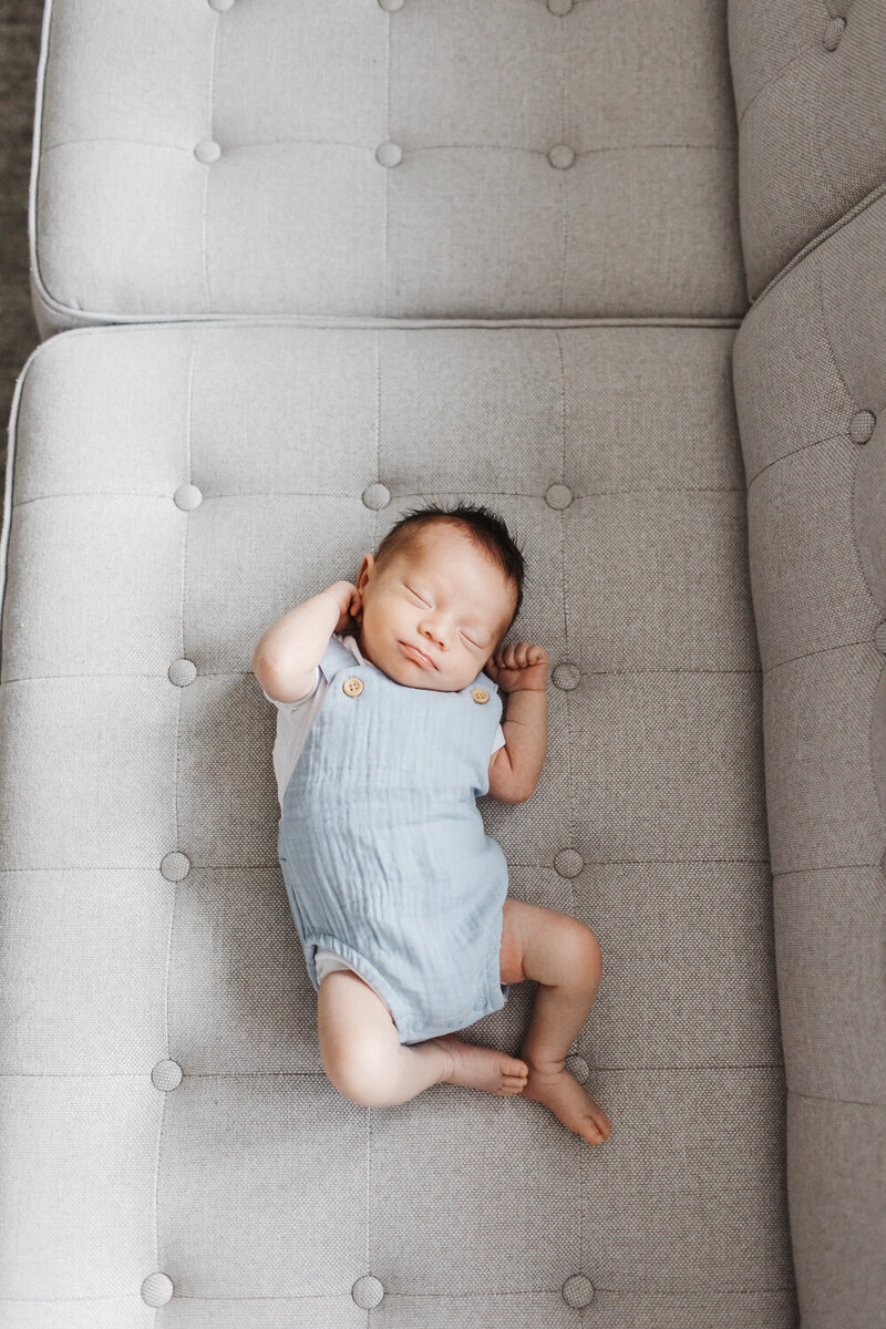 Baby boy in light blue romper sleeping on grey couch