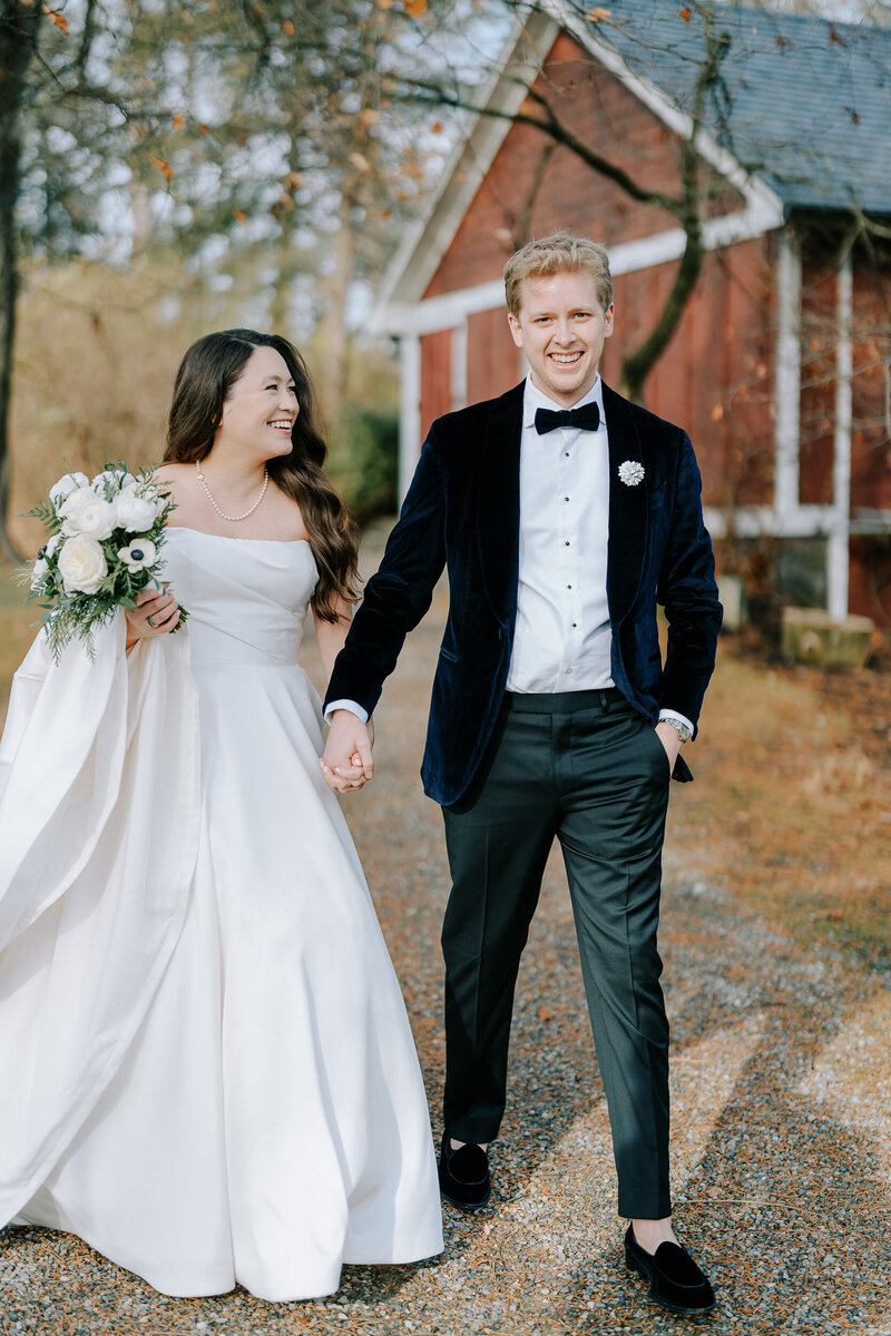 Bride and groom holding hands with an autumn leaves and red barn in the background